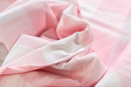 Wrinkled pink and white checkered fabric surface in a soft pastel tone. The image focuses on cloth...
