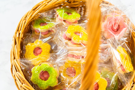 A close-up of a basket filled with vibrant Easter Cookie Sandwiches with Raspberry Buttercream in yellow, pink, and green, all individually wrapped. Great for springtime recipe visuals or festive dessert content.の写真素材