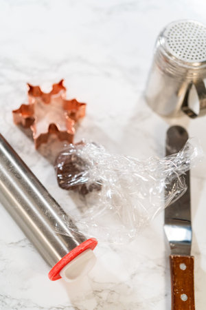 Close-up of tools and ingredients for Chocolate Ginger Sugar Cookies. A wrapped dough ball,...