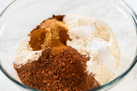 Mixing dry ingredients for Chocolate Gingerbread Cookie Dough, including flour, cocoa powder, cinnamon, ground ginger, and cloves in a glass bowl. The ingredients are layered and ready to be combined, creating a rich, aromatic base for the cookie dough.の写真素材