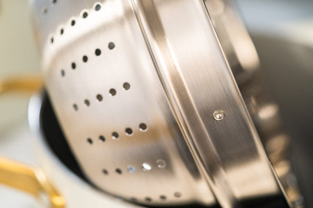 Close detail of a stainless steel steamer insert placed inside a white pot, showing texture and depth. Ideal for product features, catalogs, and cookware marketing.の写真素材