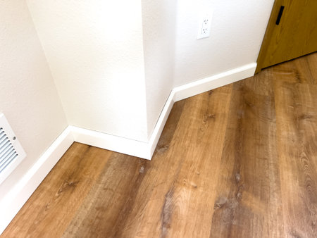 Interior photo showing clean baseboard installation against new wood-look flooring with precise corner alignment. Perfect for real estate, contractor portfolios, or DIY tutorials.の写真素材