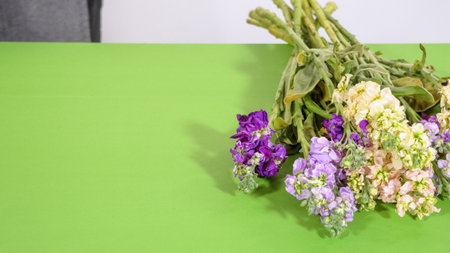 A pastel flower bouquet with pink, yellow, and purple blooms rests neatly arranged on a green table.の写真素材