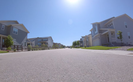 Bright morning view of a wide suburban street flanked by family homes on both sides. Strong sunlight...