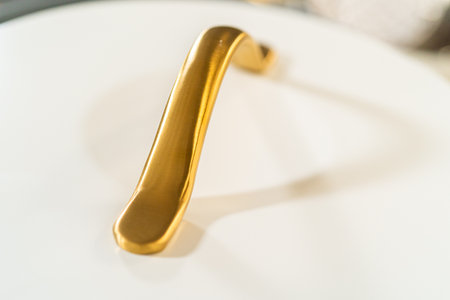 Detailed view of a curved golden handle attached to a smooth white ceramic lid. The background is softly blurred to focus on the handle design.の写真素材
