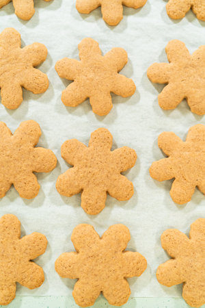 Close-up angled view of golden-brown snowflake-shaped amber gingerbread cookies cooling on parchment paper after baking, showing detailed cookie texture.の写真素材