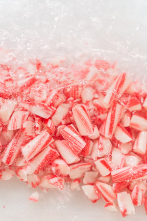 A close-up view of crushed candy canes scattered on a plastic bag, showcasing finely chopped red and white pieces for baking preparation. The perspective emphasizes texture and detail.の写真素材