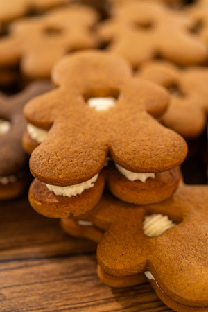 Making gingerbread man cookie sandwiches filled with eggnog buttercream, arrayed on a rustic wooden...