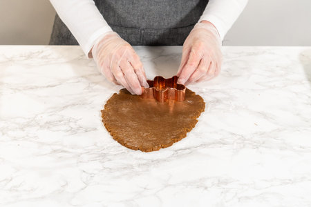 Front-facing view of a gingerbread man cookie cutter pressed into spiced gingerbread dough on a...