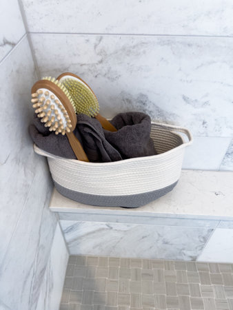 Zoomed-in image of a two-tone woven basket filled with gray towels and natural bristle brushes,...