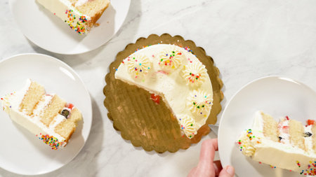 Overhead view of a party cake with white frosting and sprinkles, partially sliced and served on...