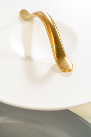 Closeup shot of a vertical gold handle attached to a matte white cookware lid.の写真素材