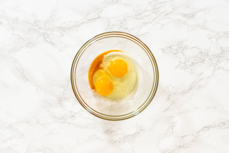 Glass bowl with beaten eggs and vanilla extract for Classic Sugar Cookie Dough on a marble surface, with a whisk resting in the mixture. This step showcases the wet ingredient preparation essential for making sugar cookie dough.の写真素材