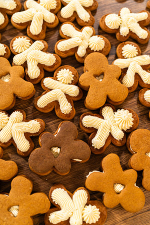 Making gingerbread man cookie sandwiches filled with eggnog buttercream, arrayed on a rustic wooden...