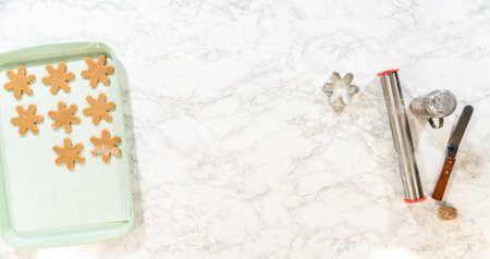 Overhead view of amber gingerbread snowflake cookies placed neatly on a green baking tray, surrounded by cookie cutters and baking tools.の写真素材