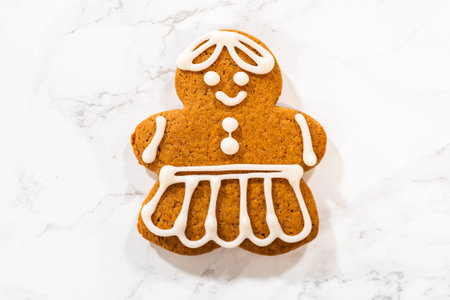 A single decorated gingerbread girl cookie on a marble countertop, showcasing its intricate royal icing dress and smiling face.の写真素材