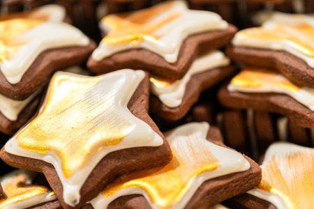 Captured from a macro perspective, a stack of golden star-shaped cookies with a rich chocolate base is elegantly decorated with white royal icing and shimmering gold accents. The intricate detailing and festive presentation make this image perfect for holiday baking promotions, bakery displays, or seasonal product packaging.の写真素材