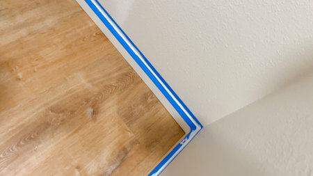 White baseboard along a corner has been taped with blue masking tape to protect it during wall painting. The tape runs neatly along the trim.の写真素材