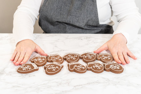 A final display of mitten-shaped gingerbread cookies fully decorated with intricate white icing patterns, arranged neatly on a marble surface.の写真素材