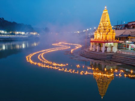 A riverside temple beautifully lit with golden lights and a path of floating diyas curving along the water. Mist in the air adds a dreamlike atmosphere to the tranquil night scene.の素材