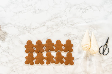 A partially decorated row of gingerbread man cookies on a marble countertop, with royal icing designs in progress.の写真素材