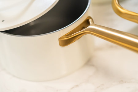 Bright image of a white saucepan with a golden handle and white lid, displayed on a kitchen counter. Great for blogs, product listings, or ads.の写真素材