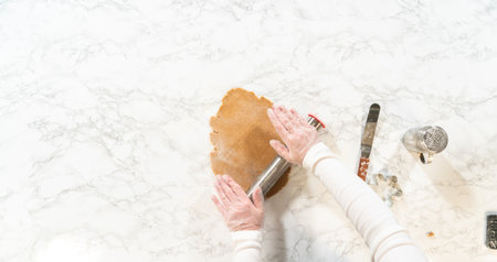 Overhead view of hands rolling out amber gingerbread dough with a rolling pin, preparing the dough for cookie cutting.の写真素材