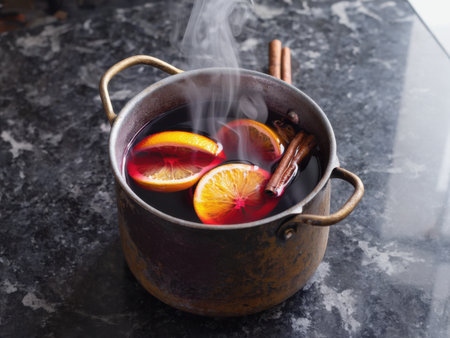 A rustic pot filled with steaming mulled wine sits on a dark stone countertop surrounded by orange slices and cinnamon sticks. The rich red tones of the wine and the natural textures create a warm and cozy holiday feeling.の素材