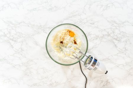 A hand mixer is used to combine eggs and other ingredients in a glass bowl, preparing for baking.の写真素材