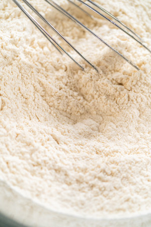 Macro image of a whisk blending flour in a glass bowl, showing the fine texture and gentle mixing. Great for food photography portfolios or baking guides. This image is part of the recipe for Classic Sugar Cookie Dough for Cutout Cookies. This image is part of the Easter Cookie Sandwich with Raspberry Buttercream recipe.の写真素材