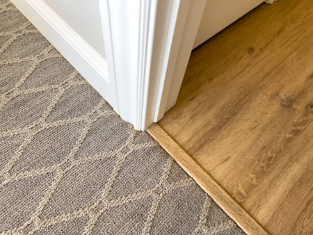 A close-up of trim work connecting patterned carpet and laminate wood flooring at a doorway. The neutral tones and clean lines reflect a well-finished modern home.の写真素材