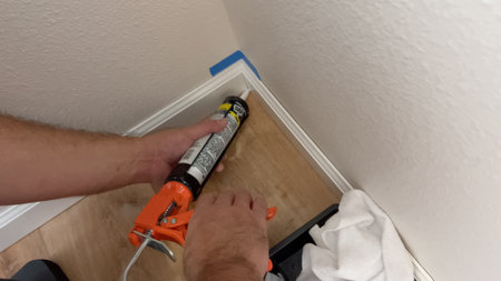Parker, Colorado, USA-November 30, 2024 - A close-up of hands using a black and orange caulking gun to apply sealant along a baseboard corner inside a home in Broomfield.のeditorial素材
