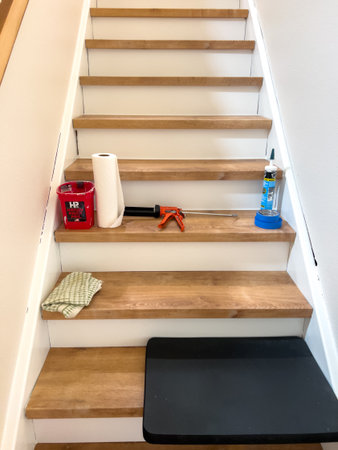 Parker, Colorado, USA-July 11, 2025 - Residential staircase with light wood steps and white risers partially remodeled. Cleaning tools, caulking gun, and a floor mat are placed on the stairs. The environment is well-lit with natural light, showing organizのeditorial素材