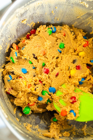 Parker, Colorado, USA-July 1, 2025 - Close-up of colorful candy-coated peanut butter cookie dough in a metal mixing bowl. A green spatula is pressed into the thick mixture, showing texture and candy details.のeditorial素材