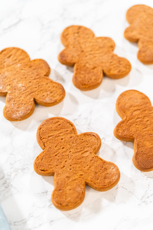 Gingerbread cookies await their second halves on a marble surface, each meticulously piped with...