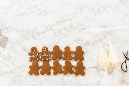 A partially decorated row of gingerbread man cookies on a marble countertop, with royal icing...