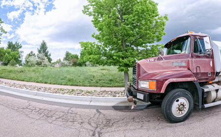 Parker, Colorado, USA-June 9, 2025 - A red commercial truck is parked along a quiet residential street with green grass and trees in the background. The road is curved and the lighting is soft under a partly cloudy sky.のeditorial素材