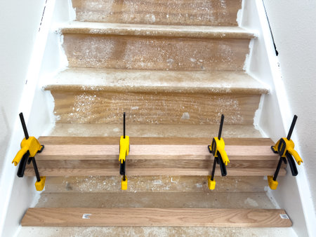 Parker, Colorado, USA-May 31, 2025 - Three new wooden stair treads are installed and held in place using several yellow clamps. The surrounding stair structure shows signs of active renovation work.のeditorial素材