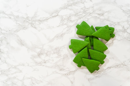 An overhead view of stacked green gingerbread cookies in the shape of Christmas trees, displayed on a marble surface. These vibrant, festive cookies add a pop of color, perfect for the Green Gingerbread Cookies recipe during the holiday season.の写真素材
