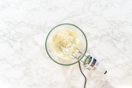 A hand mixer is used to combine eggs and other ingredients in a glass bowl, preparing for baking.の写真素材