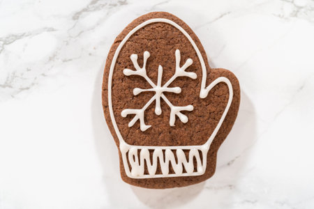A single decorated mitten cookie featuring a white royal icing snowflake and cuff design, beautifully placed on a marble background for a minimalist aesthetic.の写真素材