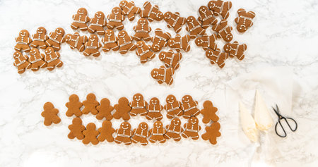 A festive arrangement of decorated gingerbread man cookies spread across a marble countertop,...