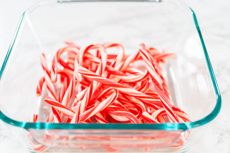 A close-up of uncrushed candy canes in a glass container, showcasing their vibrant red and white stripes for festive baking preparation.の写真素材
