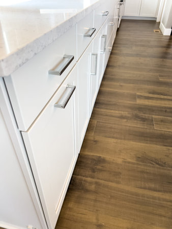A close-up of white lower kitchen cabinets with sleek silver handles and marble countertops. The wood flooring adds contrast to the bright cabinetry.