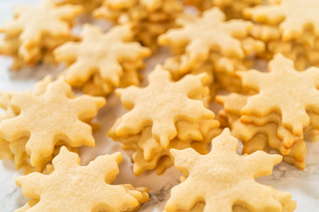 Golden, freshly baked cut-out sugar cookies shaped like festive snowflakes, cooling on a flat...