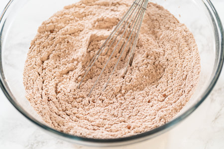 Mixing dry ingredients for Chocolate Gingerbread Cookie Dough, including flour, cocoa powder, cinnamon, ground ginger, and cloves in a glass bowl. The ingredients are layered and ready to be combined, creating a rich, aromatic base for the cookie dough.の写真素材