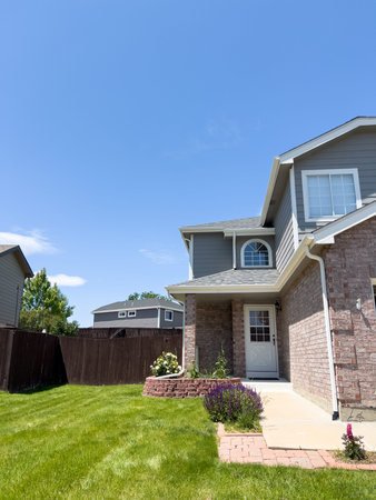 A clean suburban house with brick siding and a well-maintained front lawn. Bright sunshine...
