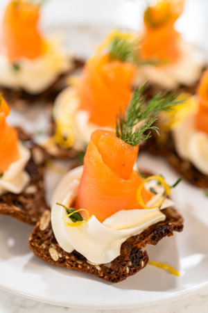 A gourmet smoked salmon canape elegantly arranged on a crispy cracker, topped with a swirl of smooth cream cheese, fresh thyme, and a drizzle of olive oil. The vibrant orange salmon contrasts beautifully with the rich, creamy base, creating a visually stunning and flavorful appetizer. Perfect for holiday gatherings, cocktail parties, or fine dining presentations.の写真素材