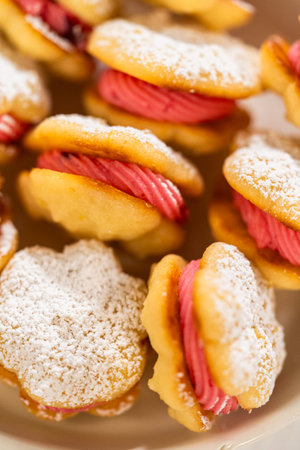 A bowl filled with lemon spritz cookie sandwiches, each piped with vibrant cranberry buttercream and...