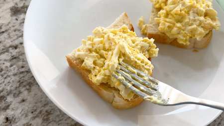 Two slices of bread are topped with creamy egg salad and served on a simple white plate.